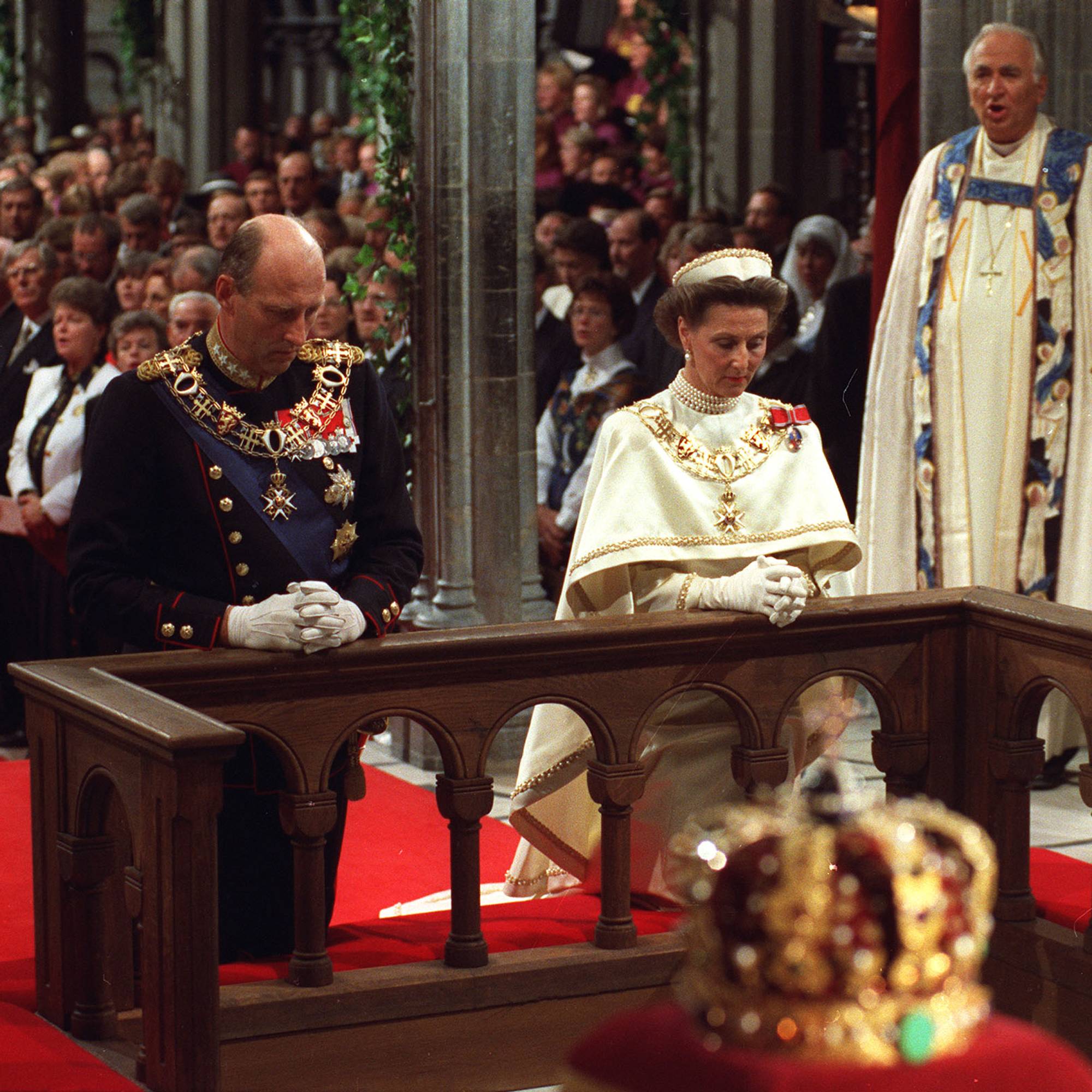 Kong Harald og dronning Sonja kneler foran alteret i Nidarosdomen under signingen av kongeparet i juni 1991. I forgrunnen sees kongekronen, som ligger på en rød fløyelsespute.