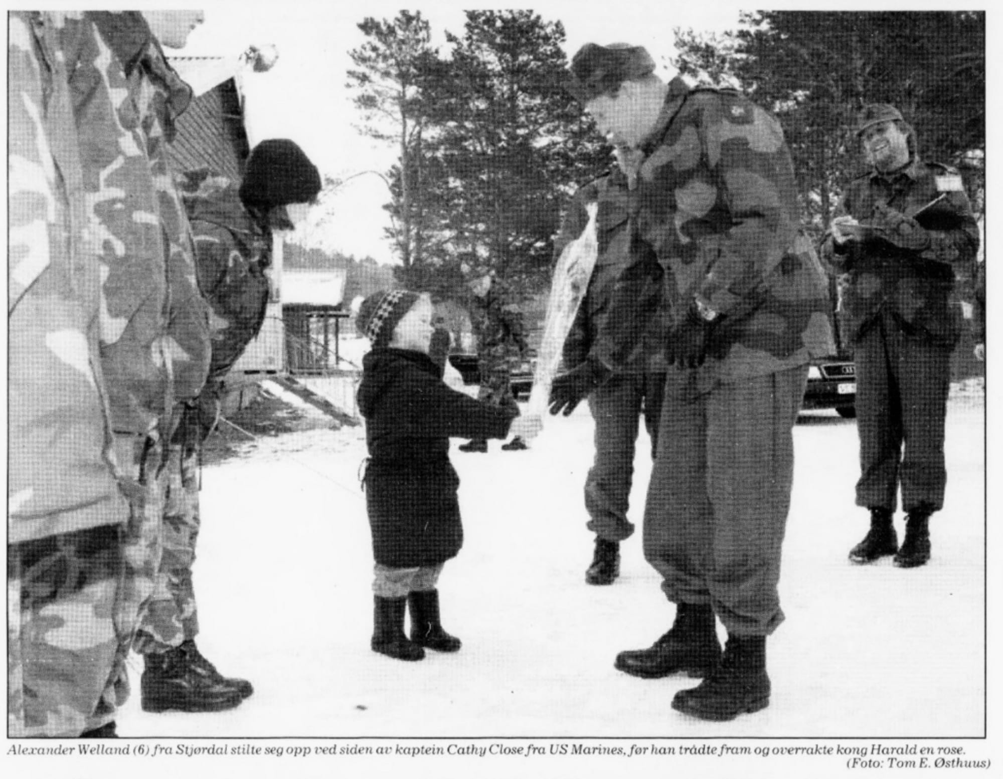 En liten gutt hilser på kongen, som er kledd i militære klær i et snødekt landskap. 