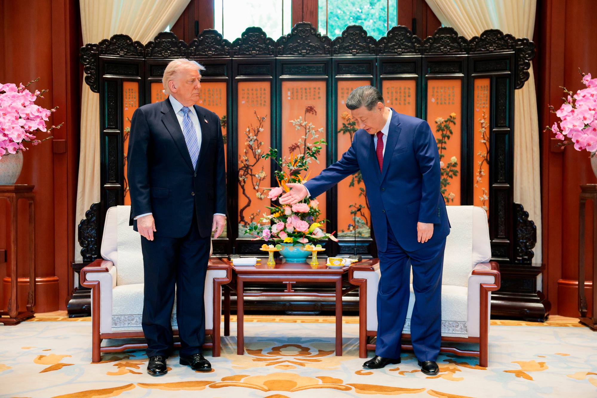 Donald Trump og Xi Jinping møtes. De står ved siden av en lavt bord med blomster og kopper. Bak dem er en tradisjonell kinesisk skjerm med dekorasjoner. (Bildebeskrivelsen er laget av en KI-tjeneste)