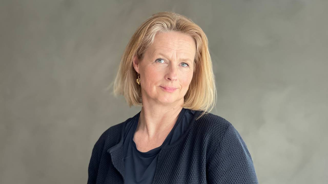 Portrettbilde av statsadvokat Unni Sandøy. Hun er iført marineblå klær, står foran en grå vegg og ser inn i kamera.