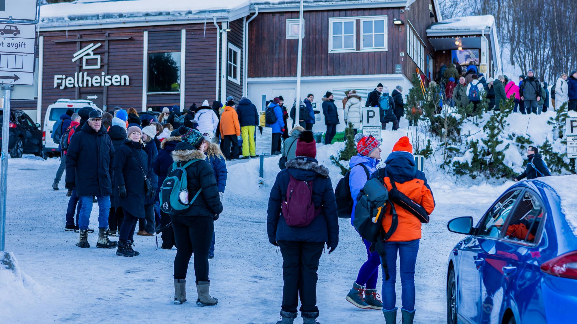 Mange mennesker står i kø foran fjellheisen i Tromsl. Det er snø på takene. Menneskene er vinterkledd