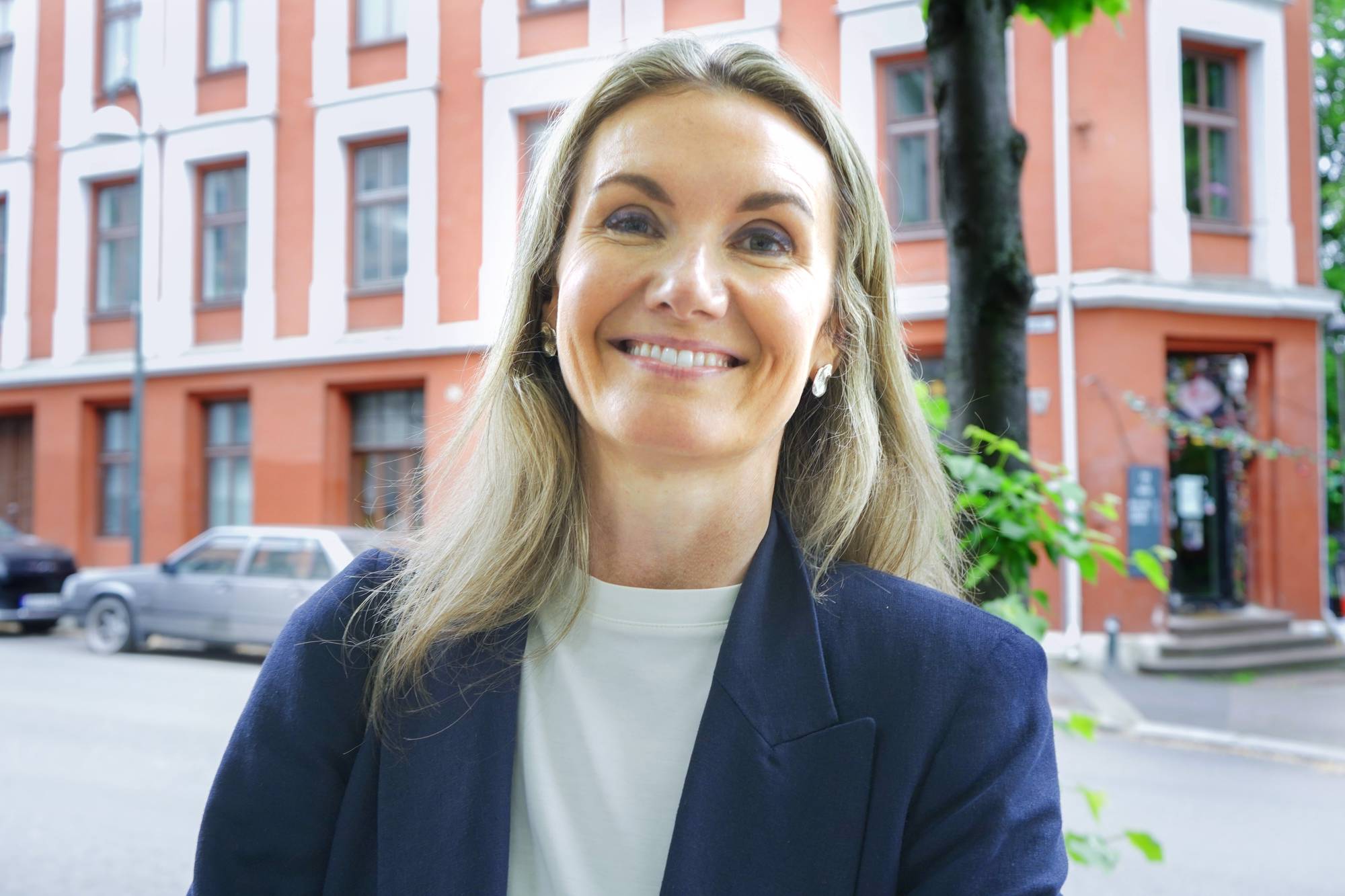 Kvinne i mørk blå blazer står føre eit leilegheitsbygg i Gamlebyen.