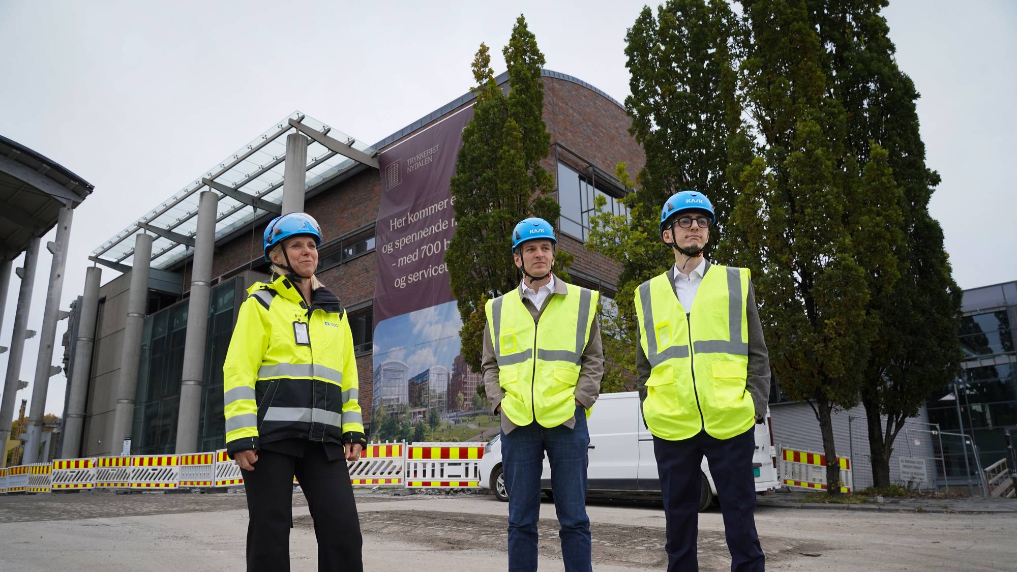 Tre personer i verneutstyr står foran en kontorbygning under oppussing i Nydalen. (Bildebeskrivelsen er laget av en KI-tjeneste)