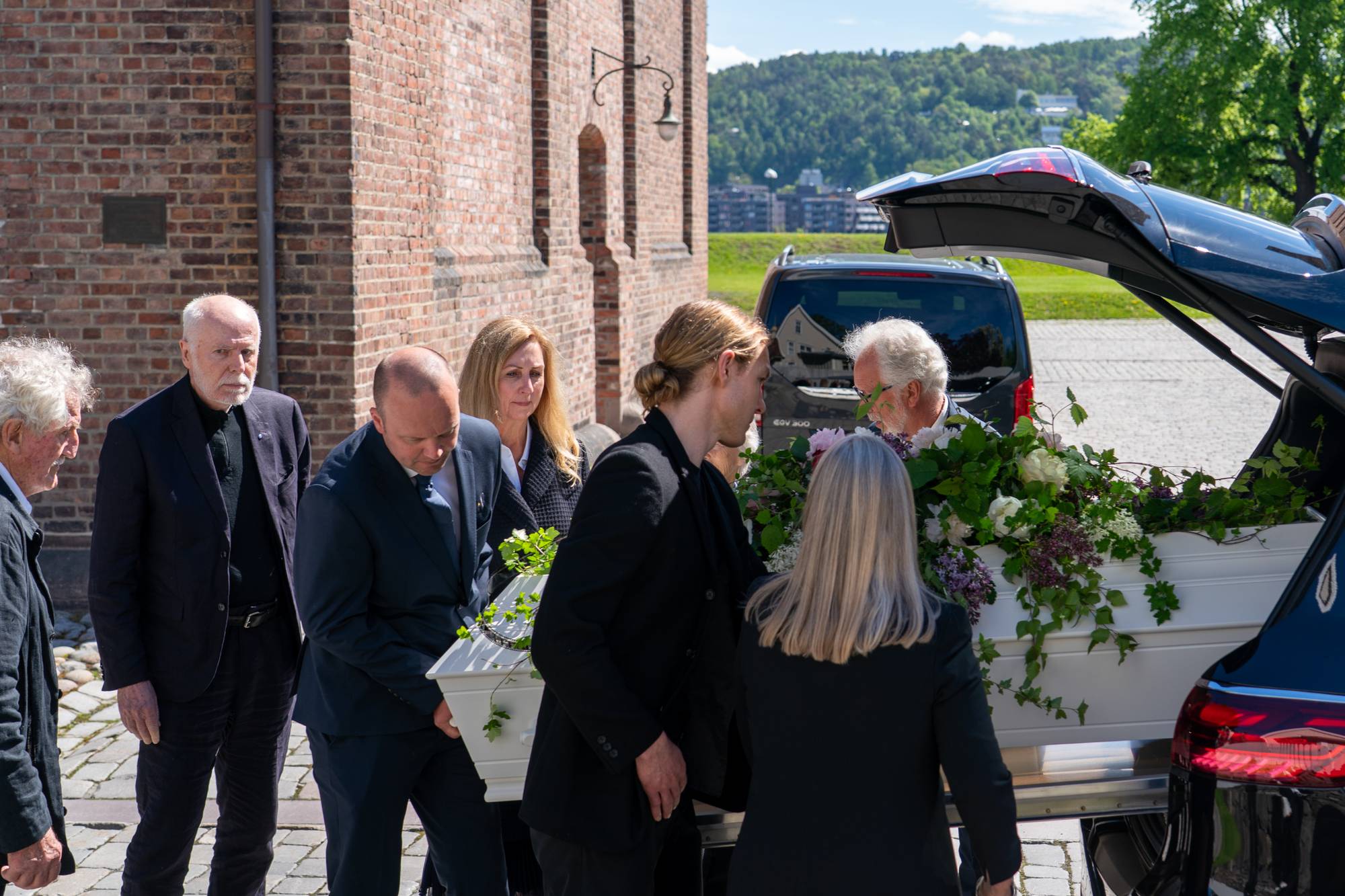 Flere personer bærer en kiste med blomster på inn i en bil. 