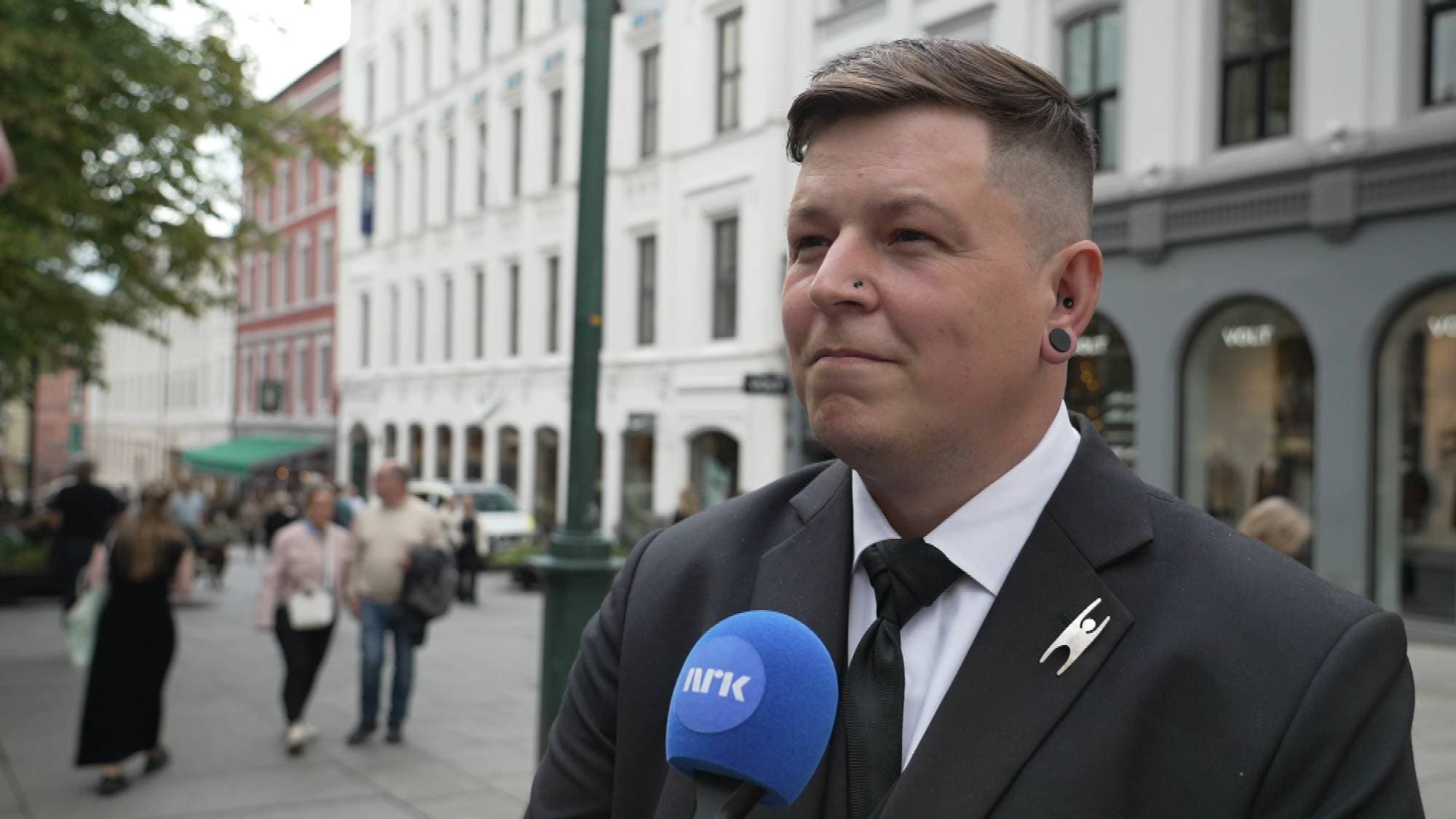 mann med kort hår i sort dress. han har human-etisk forbund sin pin på sin venstre side på jakken.