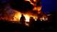 Foto: Valentyn Ogirenko / REUTERS,NTB En person i silhuett står og ser på en stor brann. En stor flamme og røyksøyle dominerer bakgrunnen. Flere bygninger og et kjøretøy er synlige i det mørke, brennende landskapet. (Bildebeskrivelsen er laget av en KI-tjeneste)