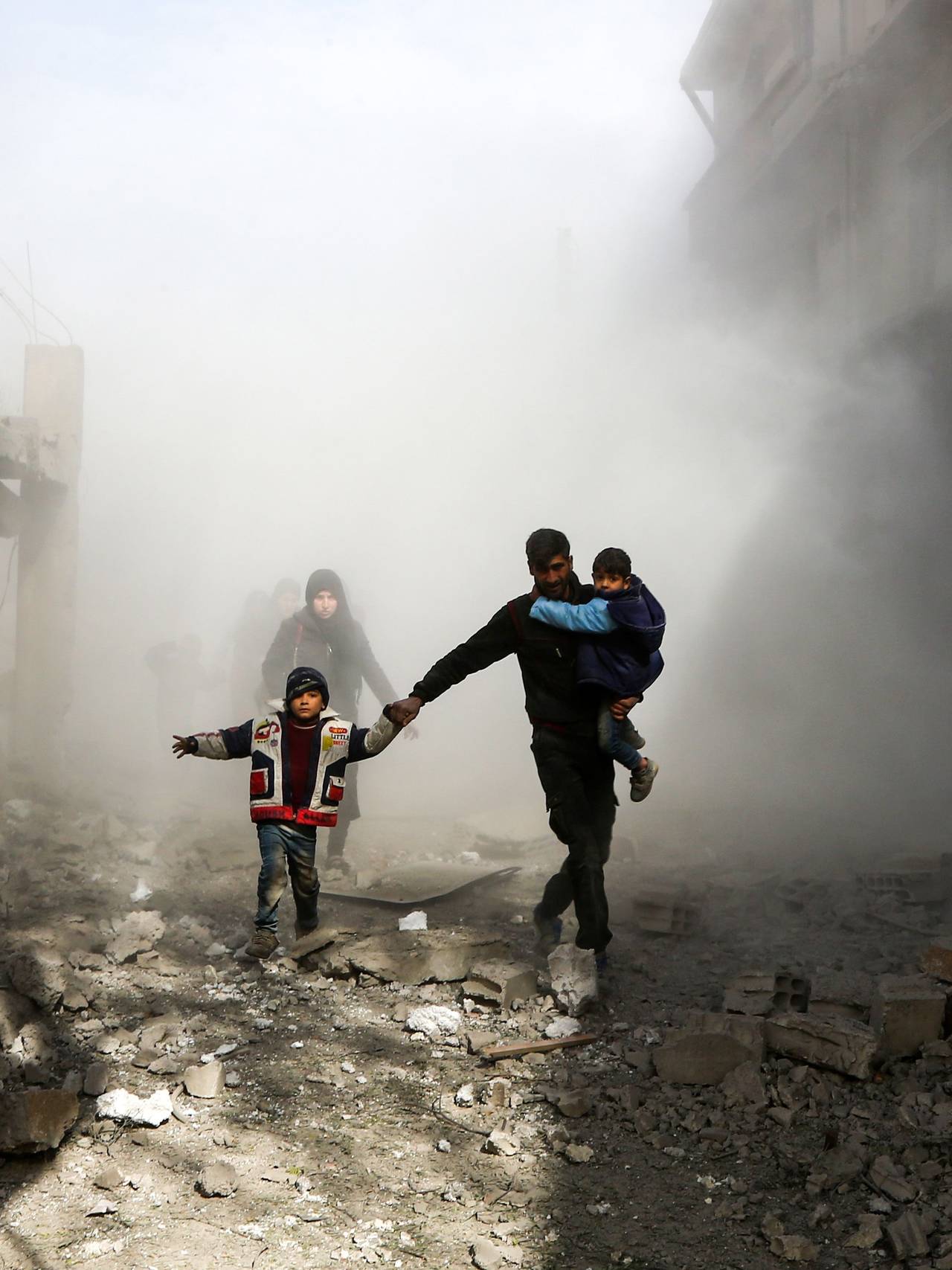 En mann med to barn løper i sikkerhet etter flyangrep i nærheten av Damaskus i Syria i 2019. 