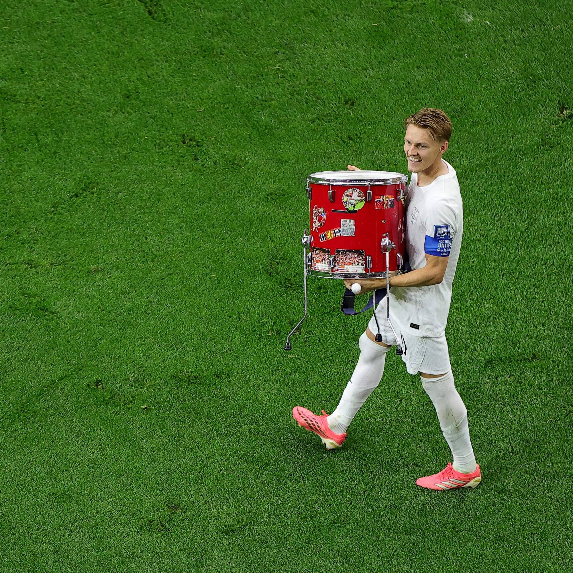 Fotballspiller Martin Ødegaard går over gressmatta med en rød tromme. (Bildebeskrivelsen er laget av en KI-tjeneste)