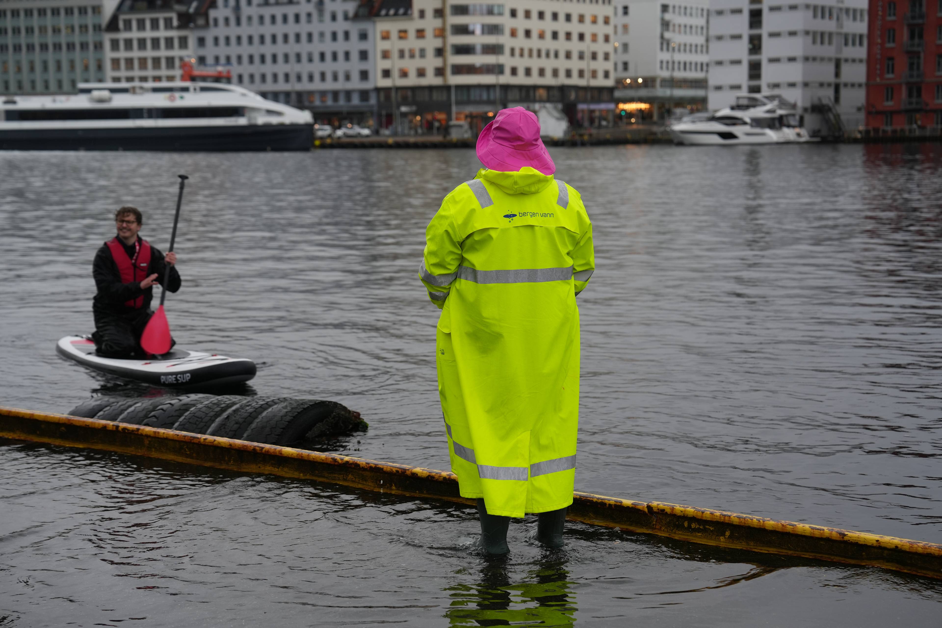 Mann som padler. En dame i gul jakke og rosa sydvest ser på.
