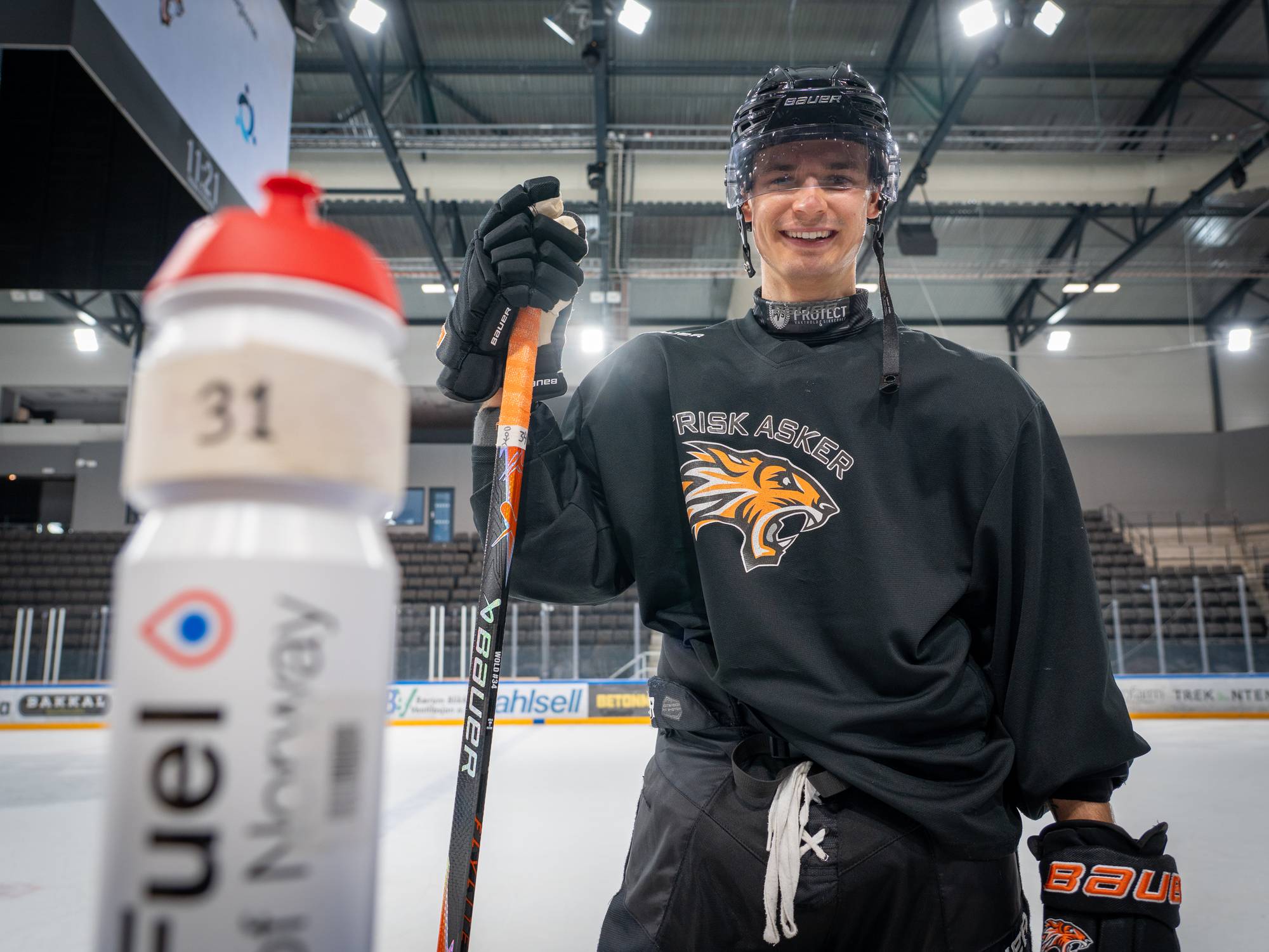 En mann i mørk hockeyuniform smiler til kamera