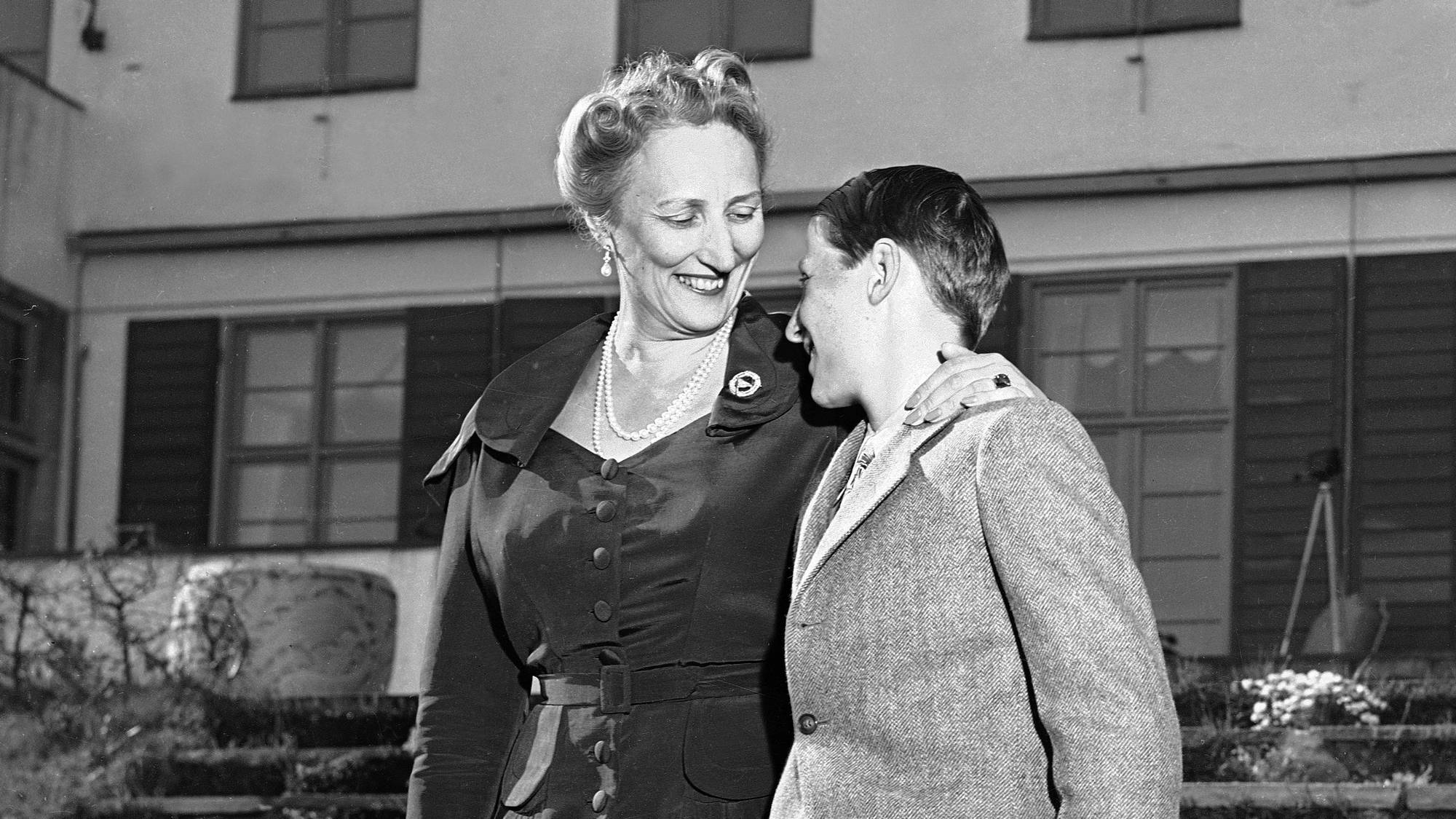 En smilende kronprinsesse Märtha legger armen rundt sønnen, prins Harald, mens de ser på hverandre 