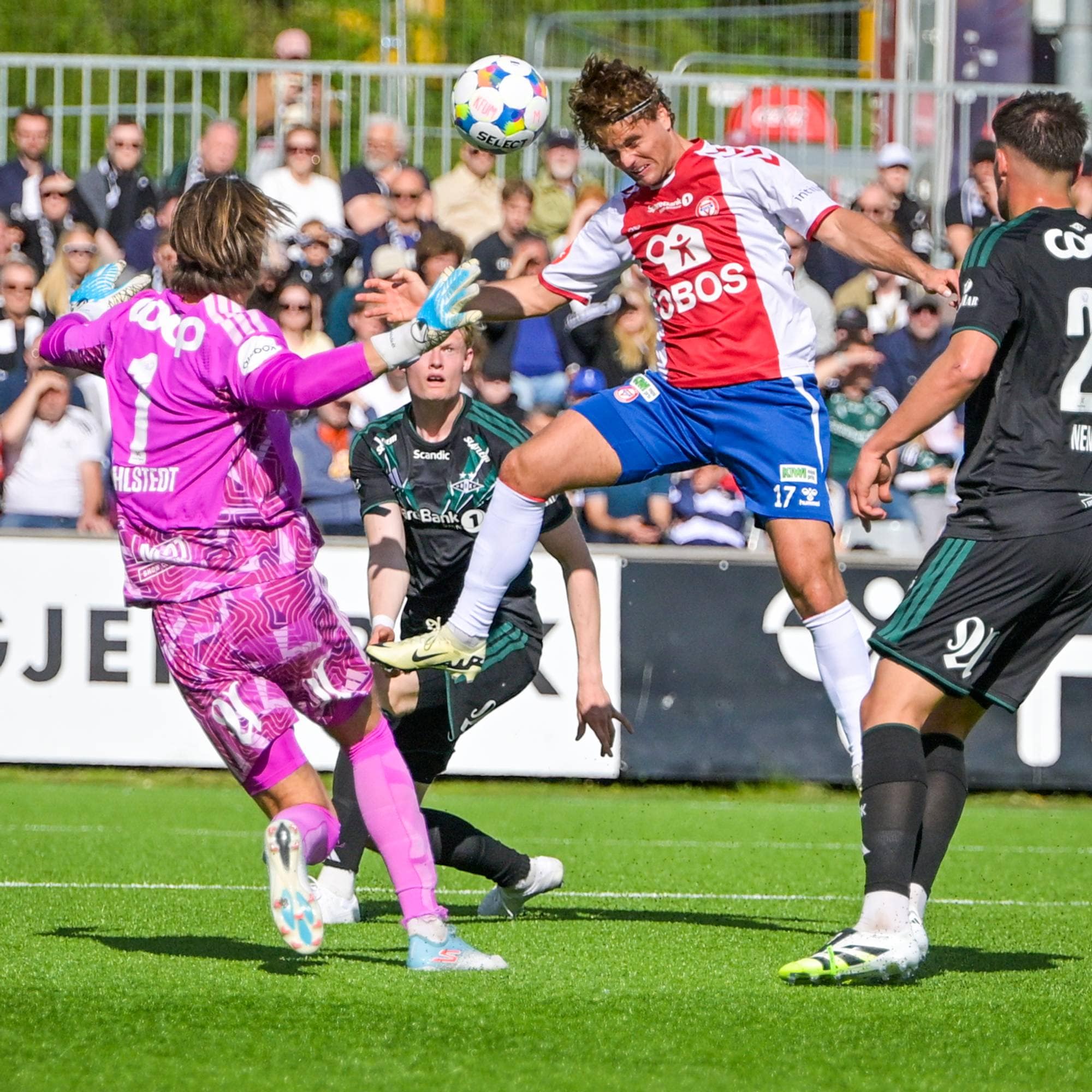 Fotballspillere kjemper om ballen i luften. En keeper i lilla drakt strekker seg for å redde. Spilleren i rød drakt header ballen. (Bildebeskrivelsen er laget av en KI-tjeneste)