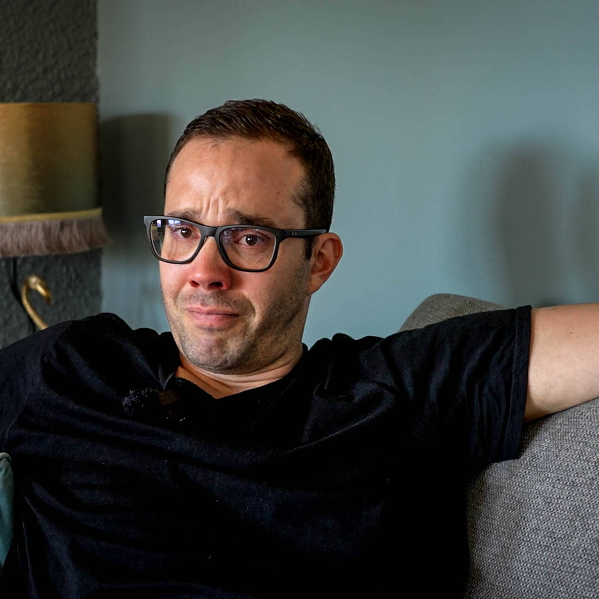 Mann sitter i sofaen og forteller