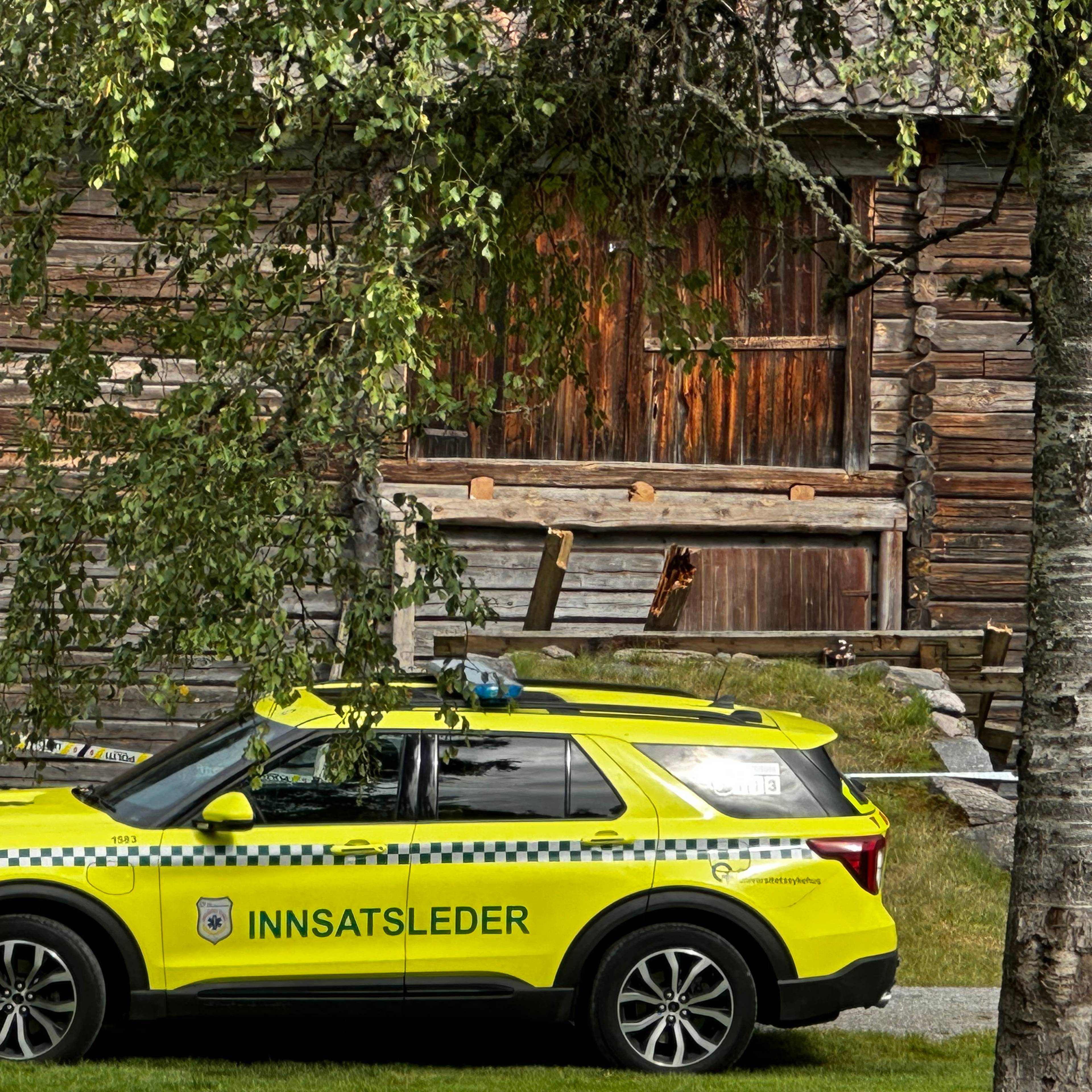 Gul innsatslederbil fra helsevesenet parkert foran en tømmerbygning sperret av med politibånd.
