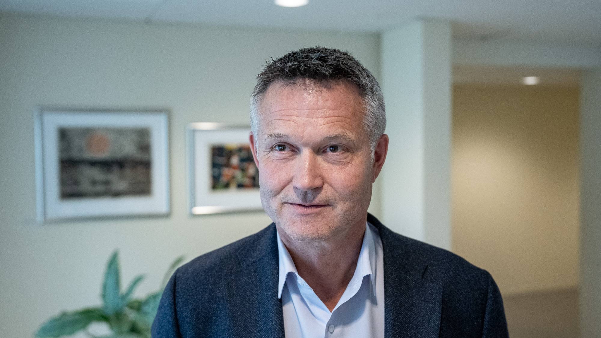 Portrett av en middelaldrende mann i dressjakke og lys skjorte, stående innendørs. (Bildebeskrivelsen er laget av en KI-tjeneste)
