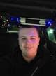 Privat En mann smiler til kamera mens han sitter inne i en bil. Det er mørkt ute og i bilen.