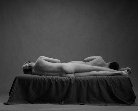 To nakne menn ligger tett inntil hverandre på senga i en omvendt ske