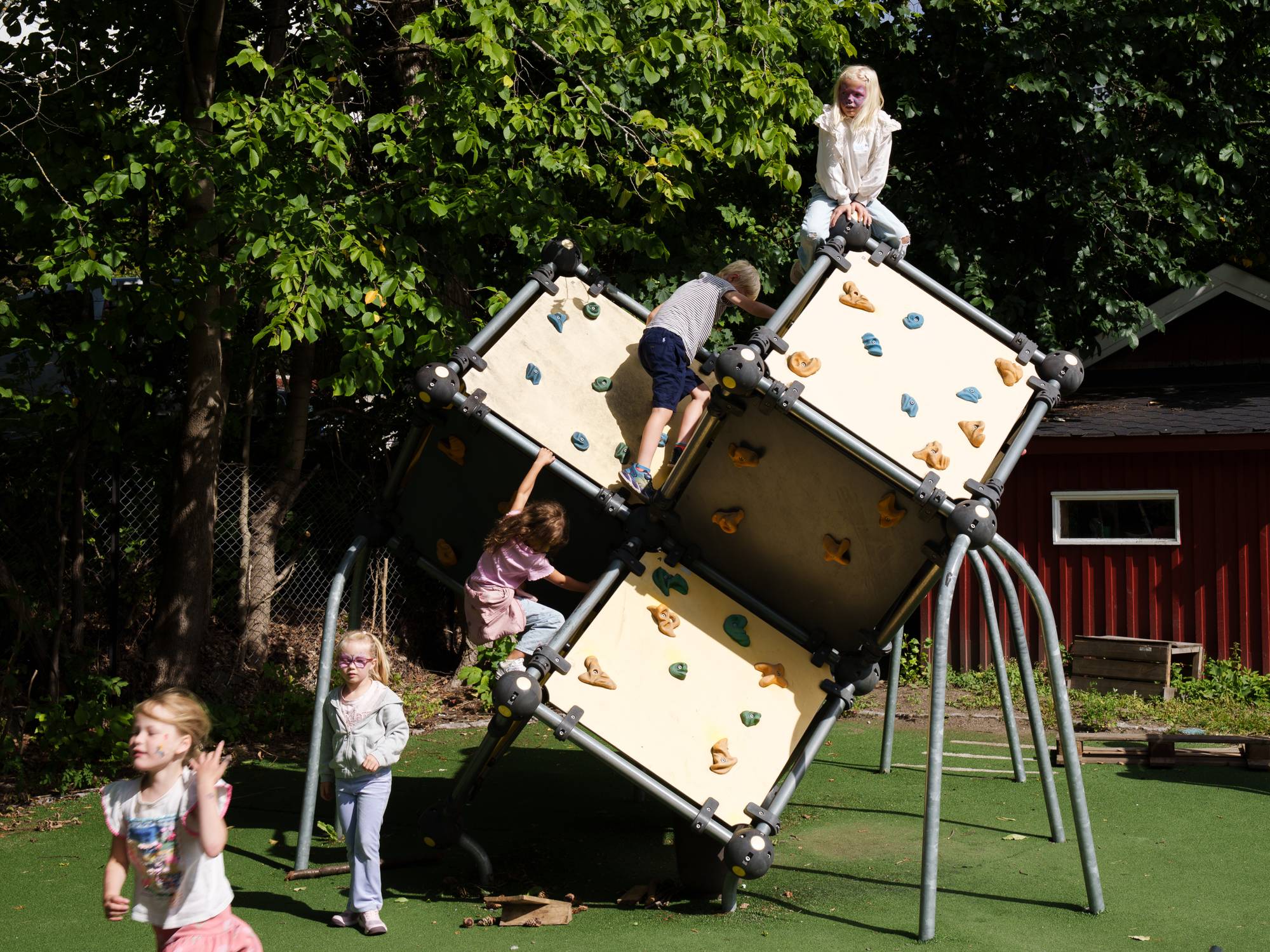 Barn leker på et klatrestativ i en park. Tre barn klatrer på stativet, mens to står på bakken. 