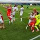MATTIA OZBOT / GETTY IMAGES NORTH AMERICA,NTB Fotballspillere kjemper om ballen under en kamp. To lag i hvite og røde drakter er tydelig synlige. Flere spillere hopper opp for å nå ballen, mens andre forsvarer seg. (Bildebeskrivelsen er laget av en KI-tjeneste)