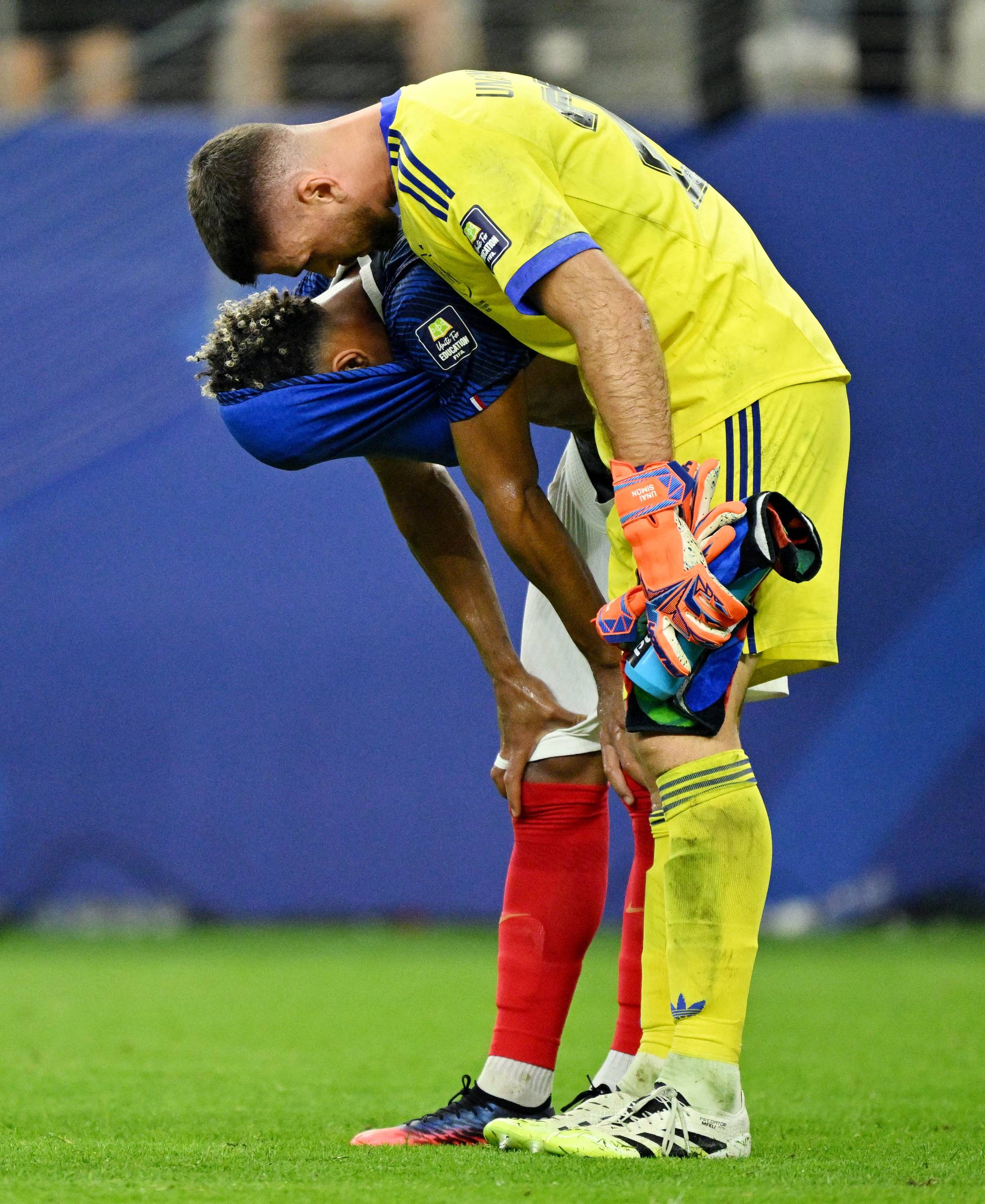 Fotballkeeper Unai Simón trøster en skuffet medspiller som har trukket drakten over hodet på banen. (Bildebeskrivelsen er laget av en KI-tjeneste)