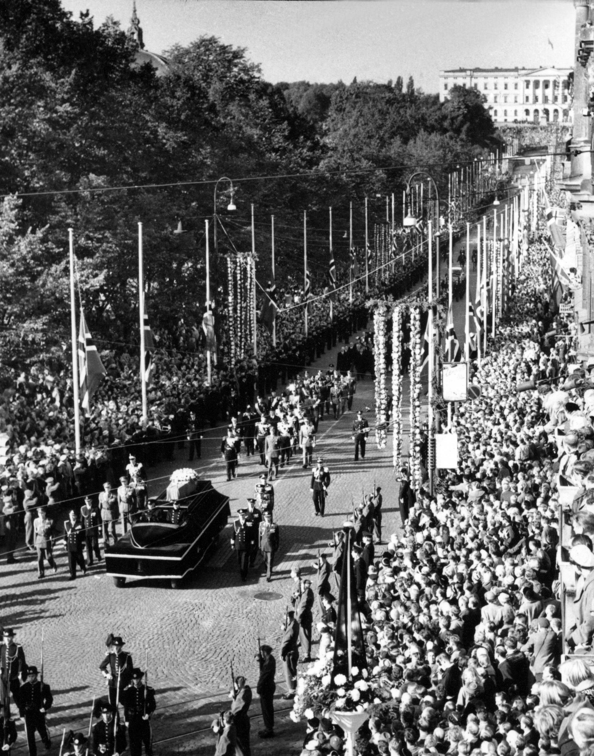 Fra Kong Haakons begravelse 21.09.1957. Oslo 19570926.Kong Haakon s begravelse. Kong Olav og kronprins Harald følger båren til fots fra Slottet til Domkirken. Her er båren på Karl Johans gate. Menneskemengder langs ruten. Slottet i bakgrunnen.FOTO SCANPIX