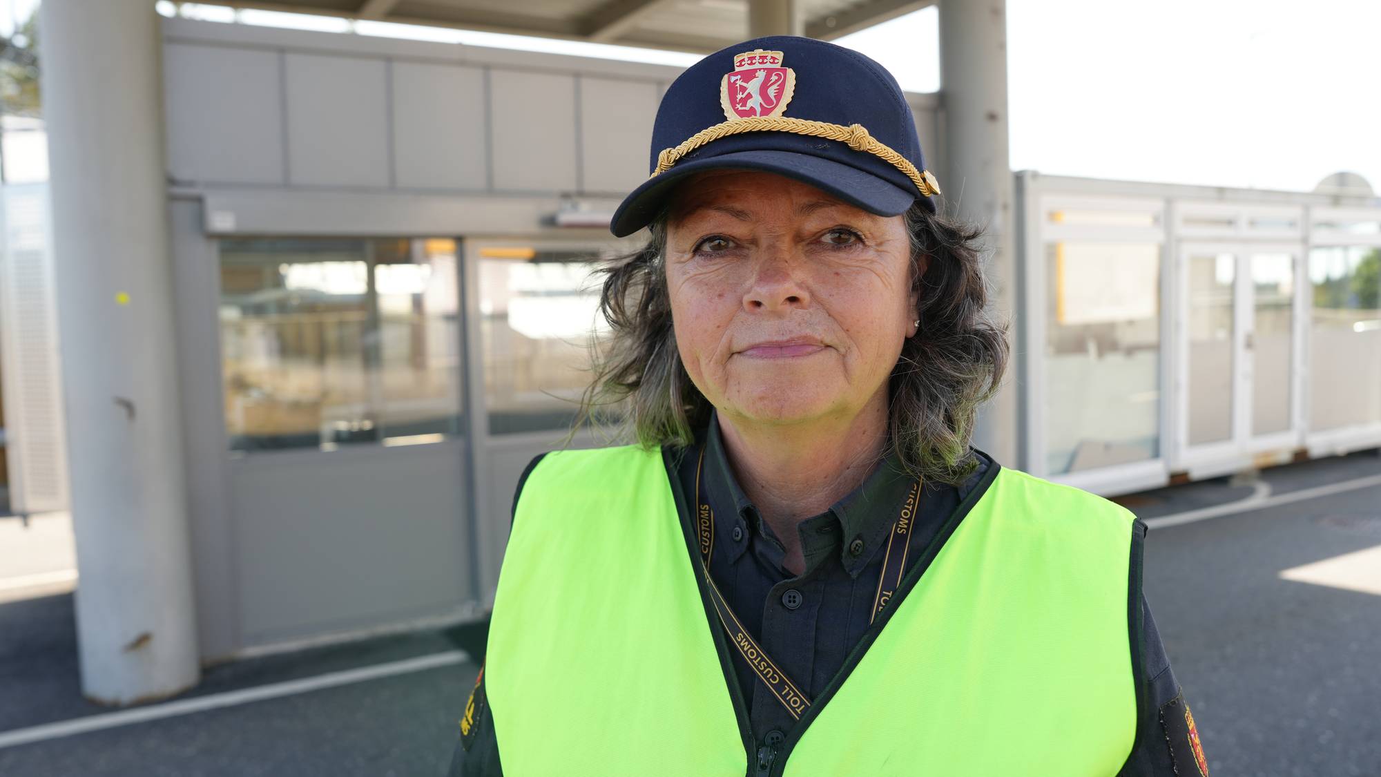 Tollbetjent i uniform og refleksvest står ved en tollstasjon. 