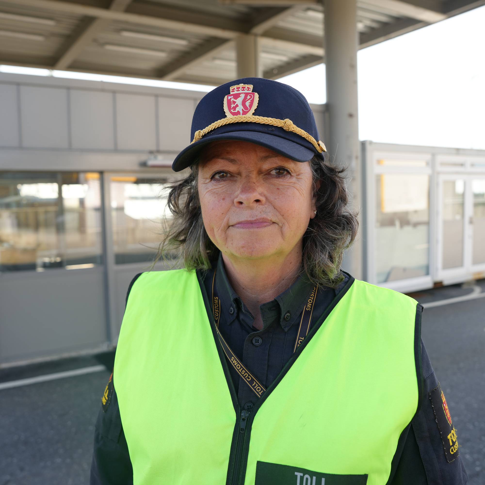 Tollbetjent i uniform og refleksvest står ved en tollstasjon. 