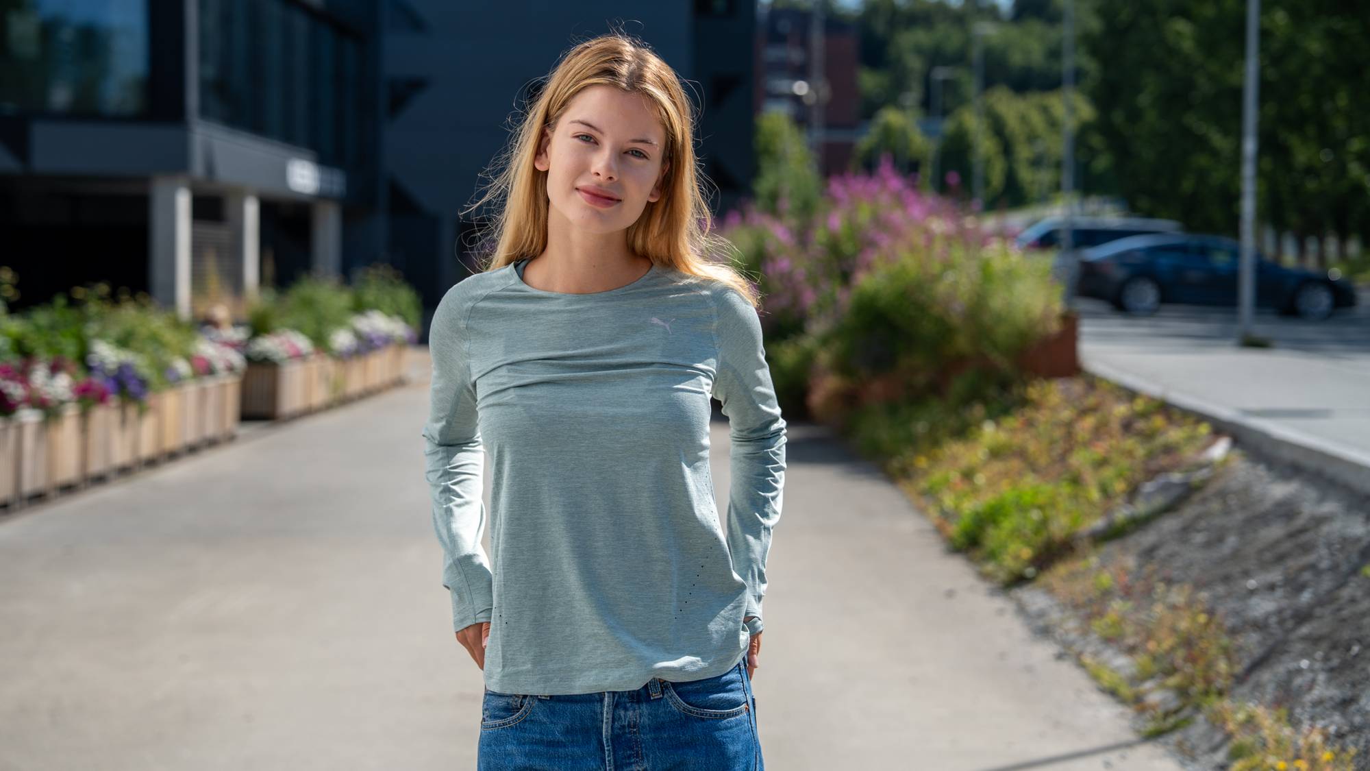 Kvinne med blondt hår står utendørs på en gangsti i en lysegrønn langermet genser og jeans. (Bildebeskrivelsen er laget av en KI-tjeneste)