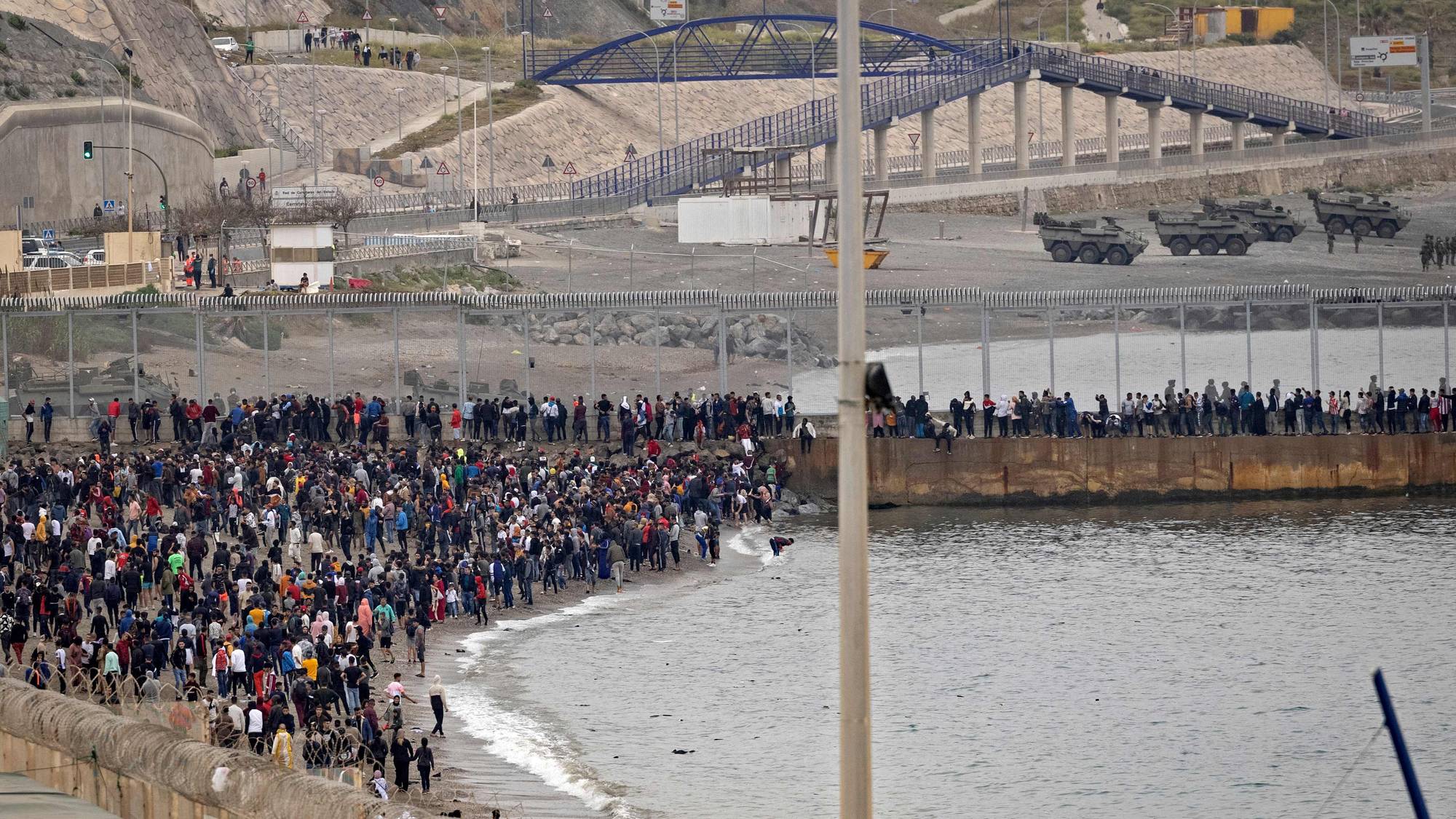 Moroccan migrants rally by a border fence in the northern town of Fnideq in an attempt to cross the border from Morocco to Spain's North African enclave of Ceuta on May 18, 2021, while Spanish troops stand to intercept them on the other side. - At least 5,000 migrants, an unprecedented influx at a time of high tension between Madrid and Rabat, slipped into Ceuta on May 17, a record for a single day, Spanish authorities said. They reached the enclave by swimming or by walking at low tide from beaches a few kilometres to the south, some using inflatable swimming rings and rubber dinghies. (Photo by FADEL SENNA / AFP)