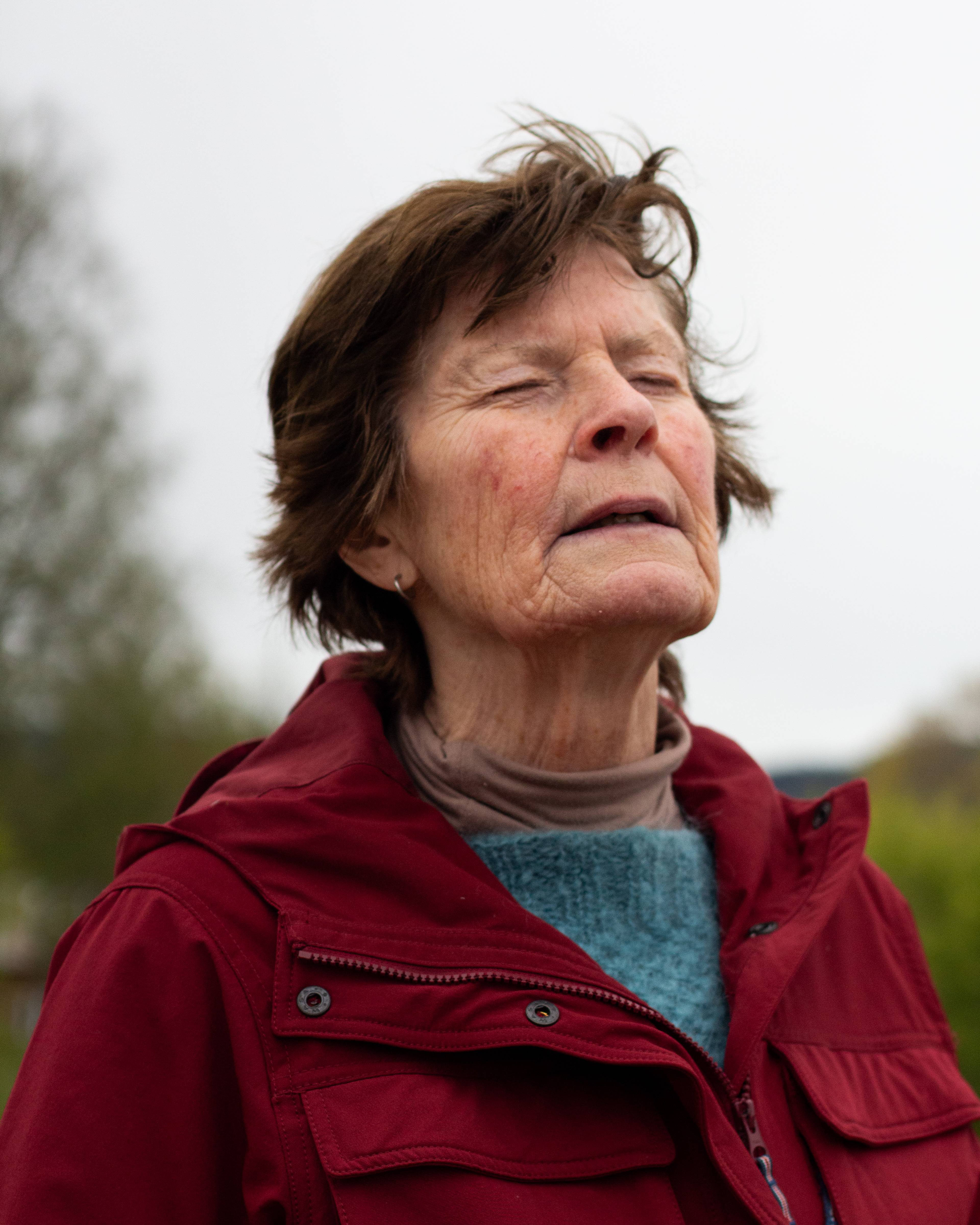 en eldre kvinne med kort brunt hår og rød jakke går rundt på et småbruk