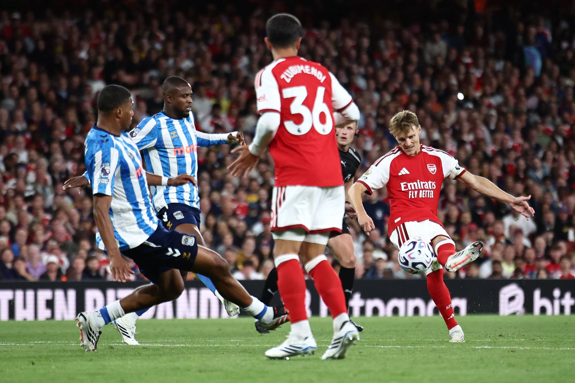 Martin Ødegaard skyter ballen i en fotballkamp mellom Arsenal og Huddersfield Town. (Bildebeskrivelsen er laget av en KI-tjeneste)