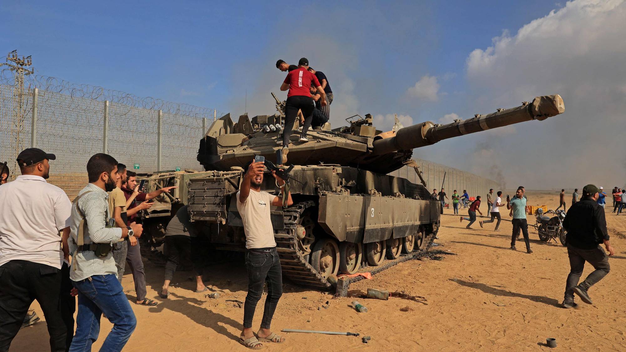 Flere menn står oppå en israelsk stridsvogn i Khan Younis etter at tusenvis av Hamas-krigere tok seg inn i Israel. 