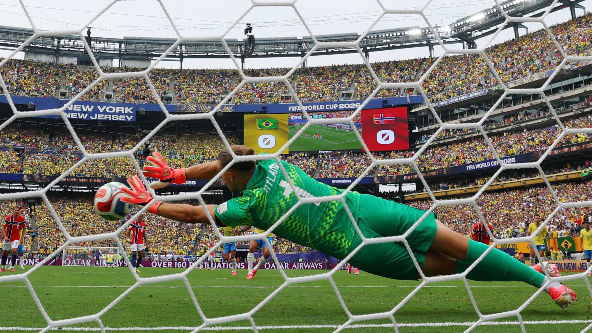 Keeper i grønn drakt kaster seg for å redde en ball foran et fullsatt stadion. Foto: NTB. (Bildebeskrivelsen er laget av en KI-tjeneste)