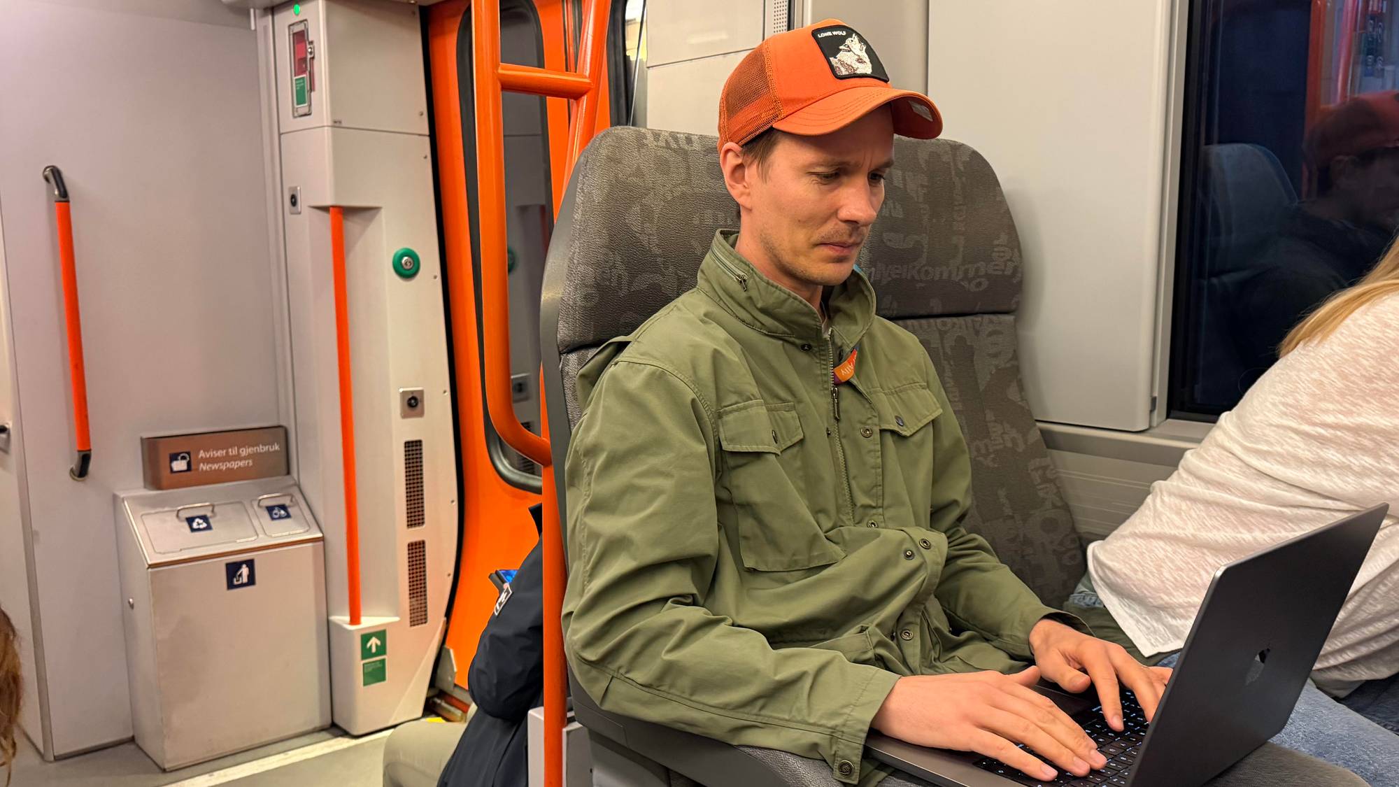 En mann med caps sitter på toget. han jobber på en PC