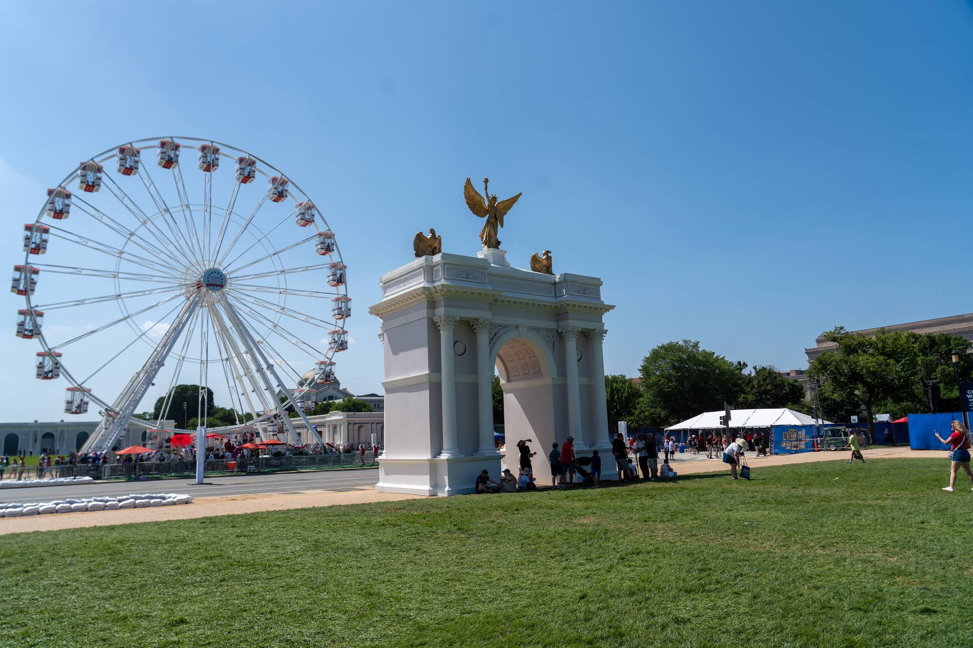 Pariserhjul og en minneportal med gullstatue på en stor gresslette med folk i Washington D.C.