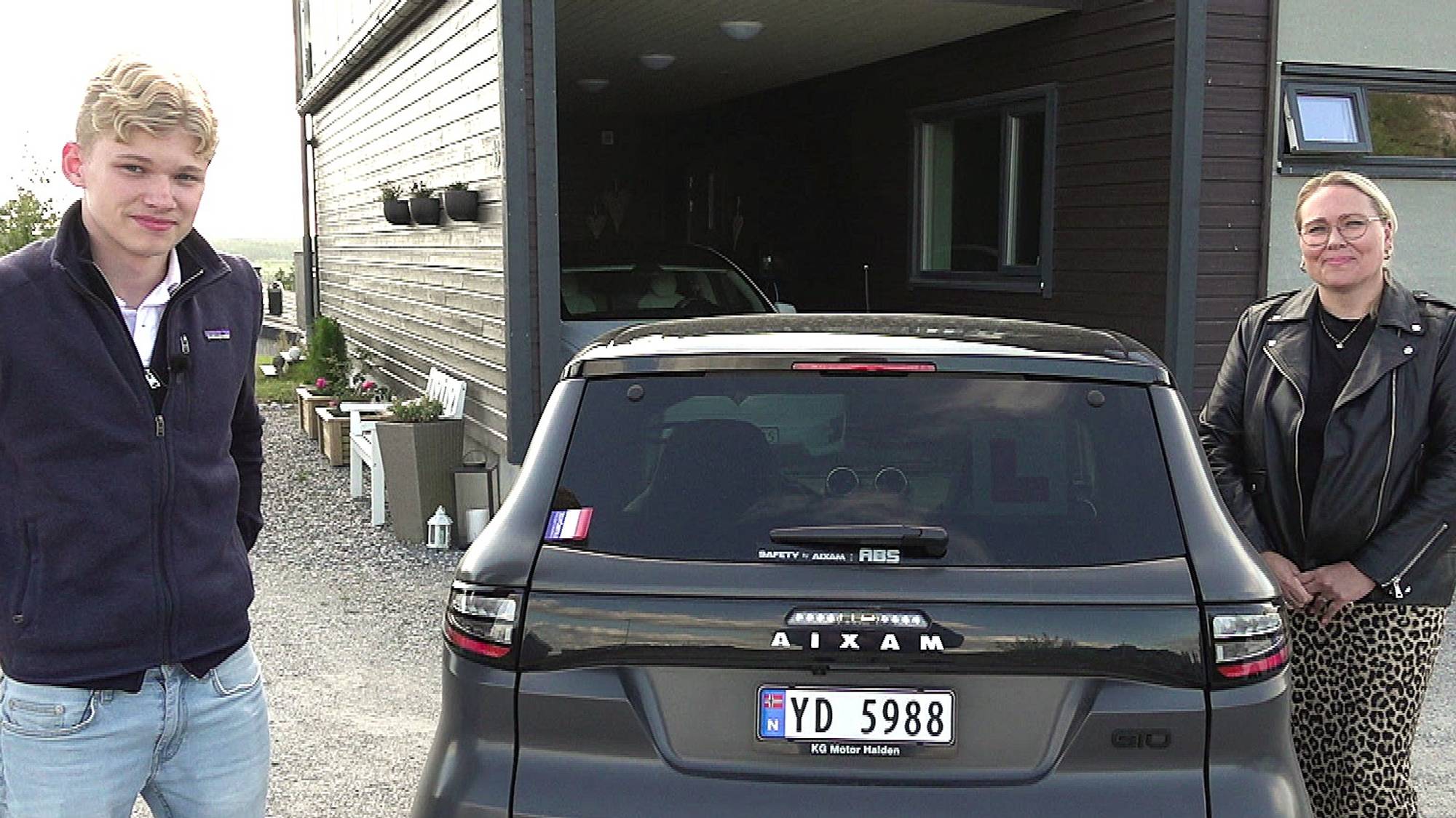 Mor og sønn står på hver sin side av sønnens mopedbil. Bilen er svart og de har på seg sommerklær
