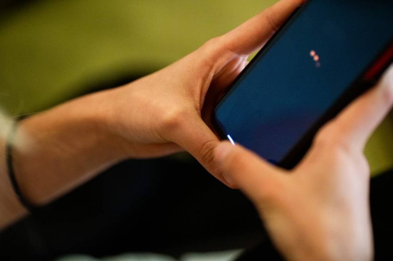 To hender holder en mobiltelefon. Skjermen er svart med to røde prikker.